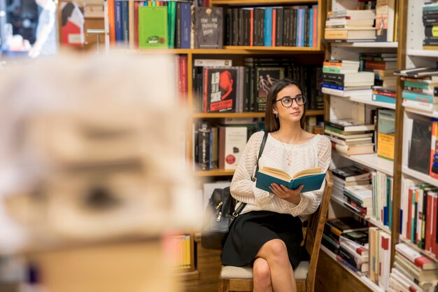 Mujer inteligente en copas sentado con el libro en la biblioteca