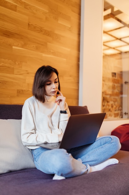 Mujer interesada en jeans y camiseta blanca está trabajando en la computadora portátil