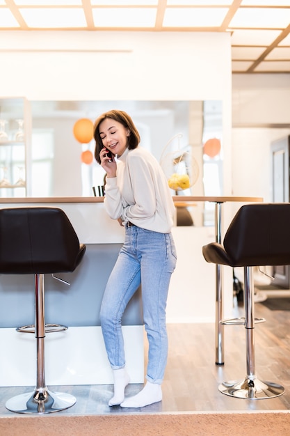 Foto gratuita mujer interesada con teléfono parado en cocina panorámica en ropa casual