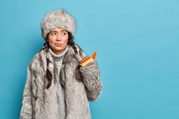 Mujer Inuit disgustada con ropa de invierno tradicional mira de mala gana y apunta hacia un espacio en blanco contra la pared azul del estudio