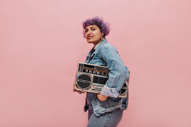 Mujer inusual con peinado morado y chaqueta de mezclilla grande y elegante y tiene radio retro.