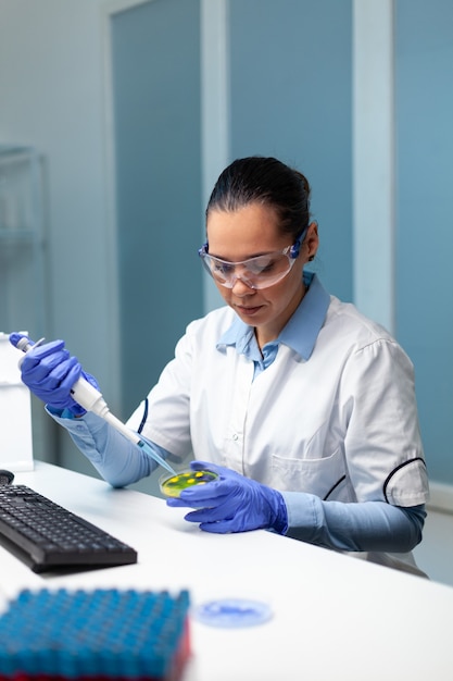 Mujer investigadora bioquímica dejando caer líquido en placa de Petri con hongos de colonia