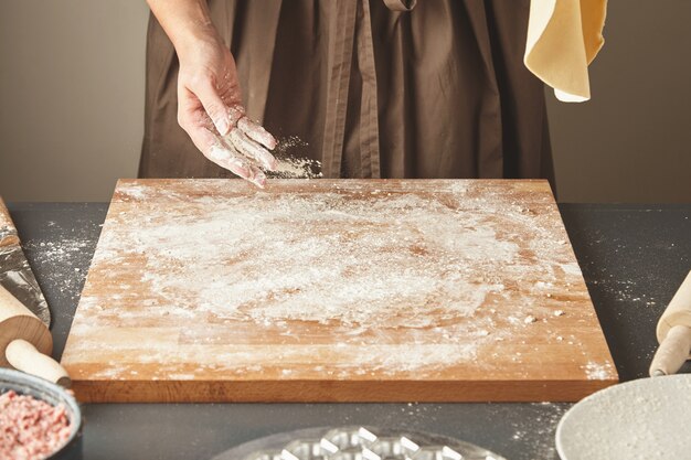 La mujer irreconocible agrega un poco de harina blanca sobre una tabla de madera mientras sostiene la masa para hacer pasta o bolas de masa en el aire. Guía paso a paso de cocción de ravioles