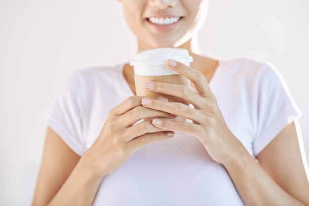 Mujer irreconocible con café para llevar con ambas manos delante del cofre