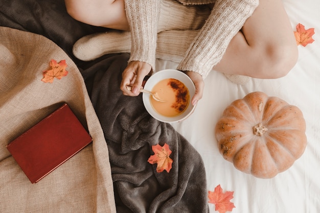 Mujer irreconocible comiendo cerca de calabaza y libro