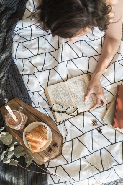 Mujer irreconocible disfrutando de la lectura durante el desayuno en la cama