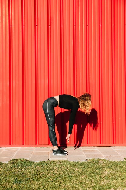 Mujer irreconocible doblándose cerca de la pared roja