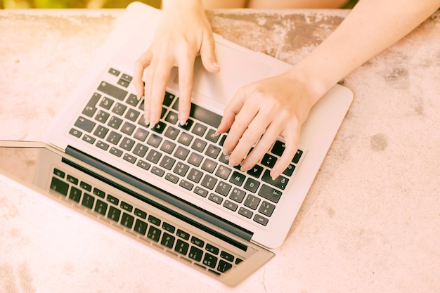 Mujer irreconocible escribiendo en el teclado del ordenador portátil al aire libre