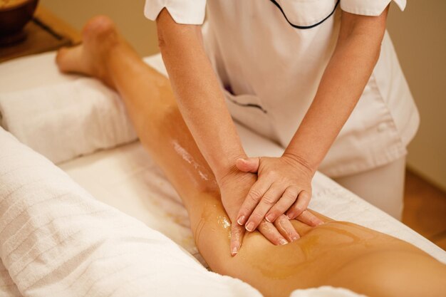 Mujer irreconocible con masaje en las piernas con miel durante el tratamiento de spa