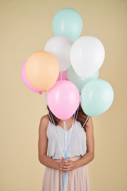 Foto gratuita mujer irreconocible posando en el estudio con la cara cubierta de globos