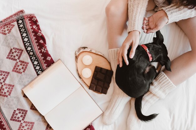 Mujer irreconocible que acaricia el perro cerca del libro y el postre