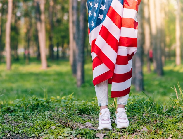 Mujer irreconocible que se coloca y que envuelve en bandera americana en naturaleza