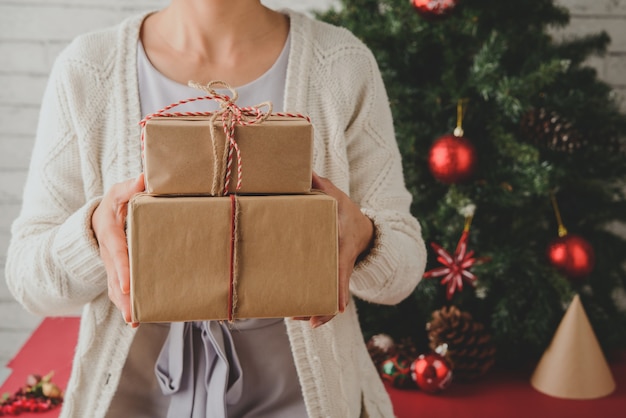 Mujer irreconocible con regalos envueltos delante del árbol de Navidad en casa