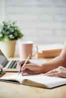 Foto gratuita mujer irreconocible sentada en el escritorio en el interior y escribiendo en planificador
