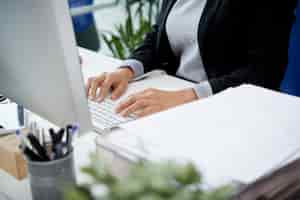Foto gratuita mujer irreconocible sentada en el escritorio en la oficina y escribiendo en el teclado