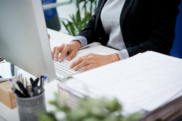 Mujer irreconocible sentada en el escritorio en la oficina y escribiendo en el teclado