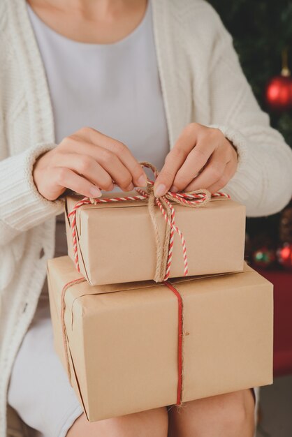 Mujer irreconocible sentada con regalos envueltos en el regazo y desatando el arco