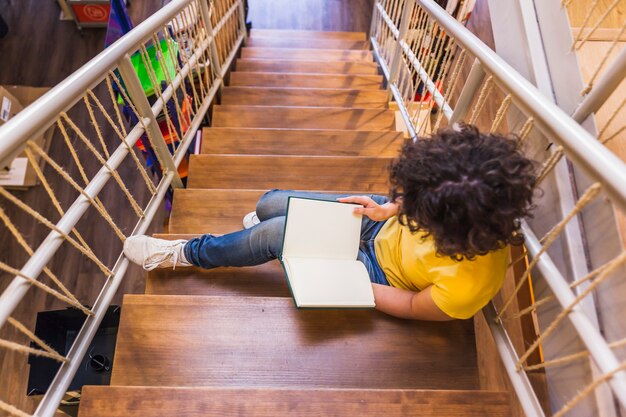 Mujer irreconocible sentado en las escaleras con el libro