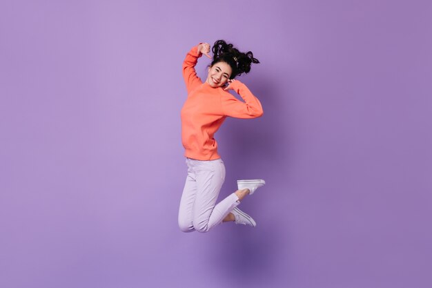 Mujer japonesa complacida saltando sobre fondo púrpura. Foto de estudio de feliz joven asiática.