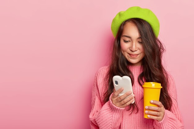 Mujer japonesa joven morena atractiva tiene teléfono móvil moderno, envía mensajes de texto en el chat en línea