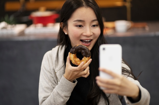 Mujer japonesa tomando selfie mientras come un donut