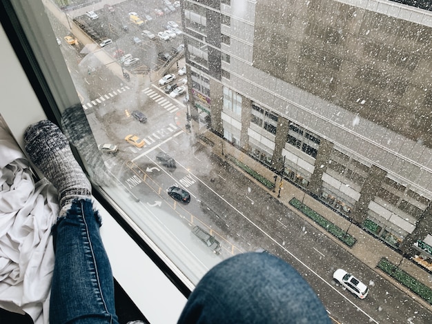 Mujer con jeans y calcetines cerca de una ventana mirando hacia las calles
