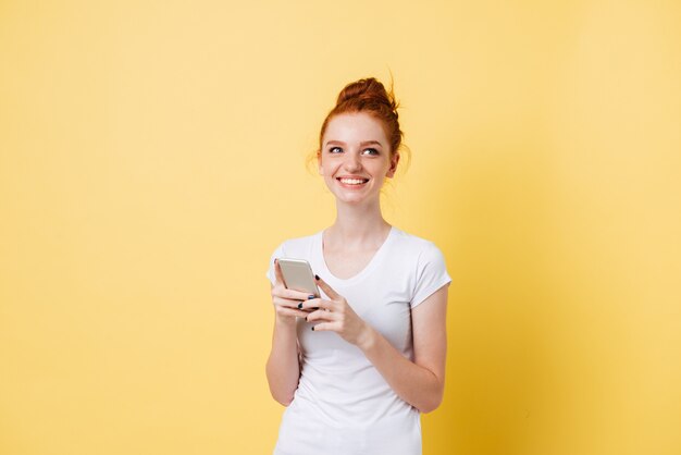 Mujer de jengibre contenta en camiseta con smartphone en manos