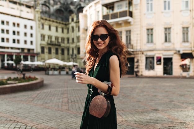 Mujer de jengibre en elegantes gafas de sol sonriendo afuera