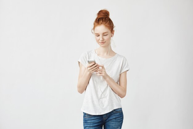 Mujer de jengibre con pecas en auriculares sonriendo mirando el teléfono.