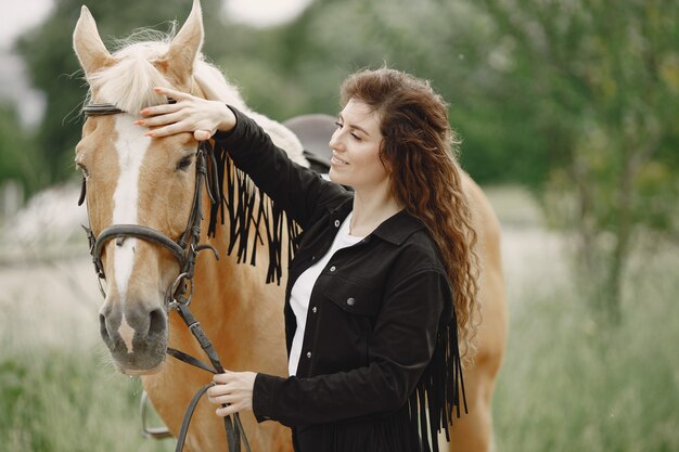 Mujer jinete hablando con su caballo en un rancho. La mujer tiene cabello largo y ropa negra. Mujer ecuestre tocando las riendas de un caballo.