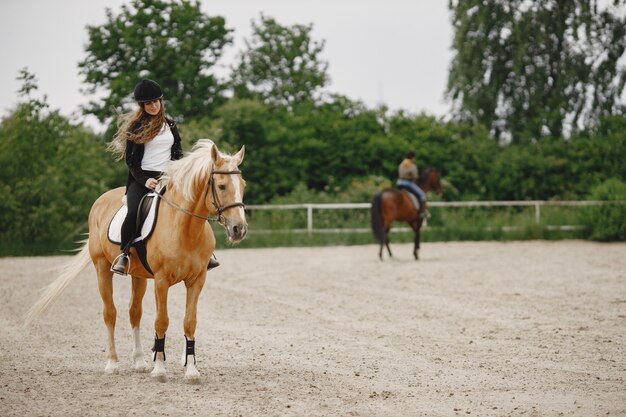 Mujer jinete montando su caballo en un rancho. La mujer tiene cabello largo y ropa negra. Segundo jinete borrosa en un caballo sobre un fondo.