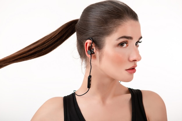 Mujer en jogging top negro escuchando música en auriculares posando aislado en blanco