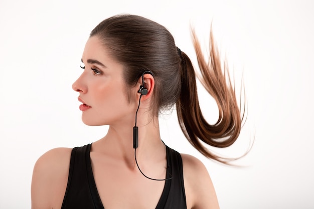 Mujer en jogging top negro escuchando música en auriculares posando aislado en blanco