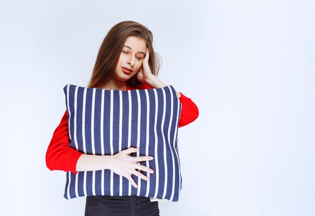 mujer joven abrazando una almohada de rayas azules y durmiendo.