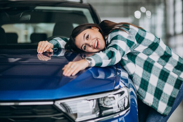 Mujer joven abrazando un automóvil en una sala de exposición de automóviles