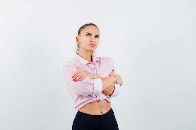 Mujer joven abrazándose a sí misma en camisa casual, pantalones y bonita vista frontal.