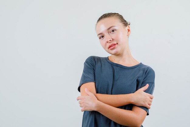 Mujer joven abrazándose a sí misma en camiseta gris y mirando esperanzada