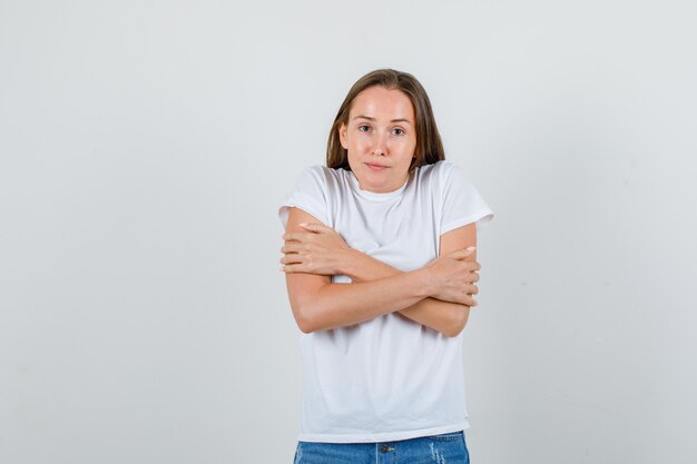 Mujer joven abrazándose y sintiendo frío en camiseta blanca, vista frontal de pantalones cortos.