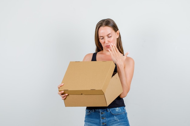 Mujer joven abriendo y mirando en una caja de cartón en camiseta, pantalones cortos y mirando molesto