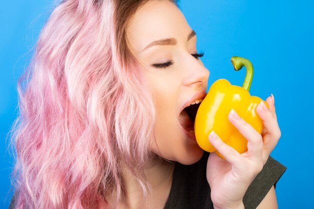 Mujer joven abriendo su boca para morder un pimiento amarillo