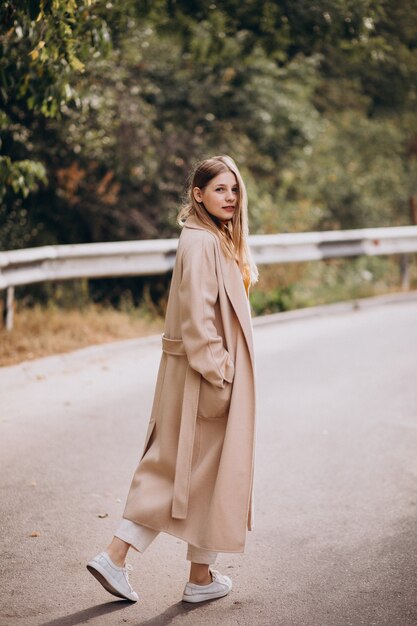 Mujer joven en abrigo beige caminando en el parque