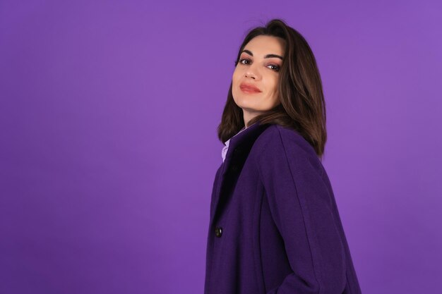 Mujer joven con un abrigo de lana sobre un fondo morado posando, acogedor y cálido, estilo otoño-invierno, sonriendo con confianza con lápiz labial en los labios