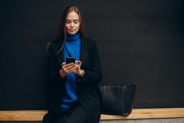 Mujer joven, en, abrigo negro, utilizar, teléfono