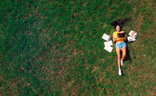 mujer joven acostada en un prado verde lee libros