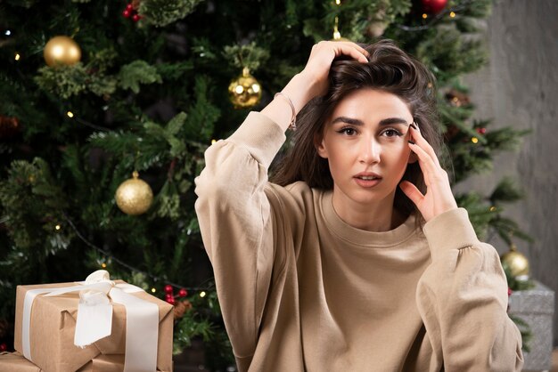 Mujer joven acostada sobre una alfombra mullida cerca del árbol de Navidad.