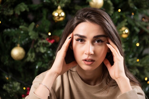 Mujer joven acostada sobre una alfombra mullida cerca del árbol de Navidad.