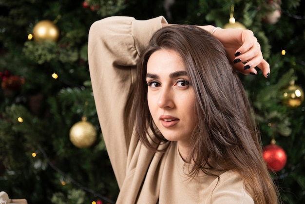 Mujer joven acostada sobre una alfombra mullida cerca del árbol de Navidad.