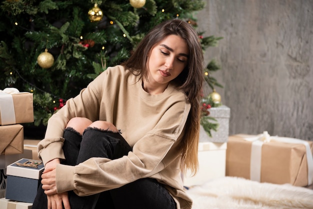 Mujer joven acostada sobre una alfombra mullida con regalos de Navidad.