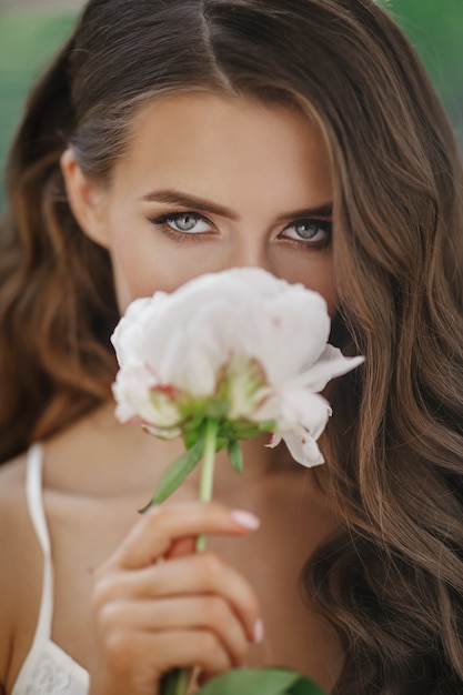 La mujer joven adorable sostiene la flor blanca antes de su cara