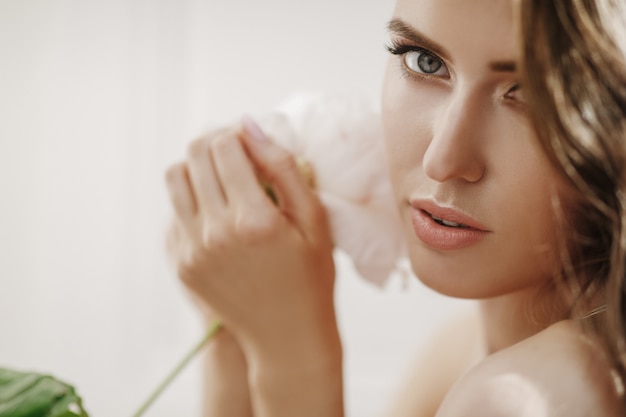 La mujer joven adorable sostiene la flor blanca antes de su cara